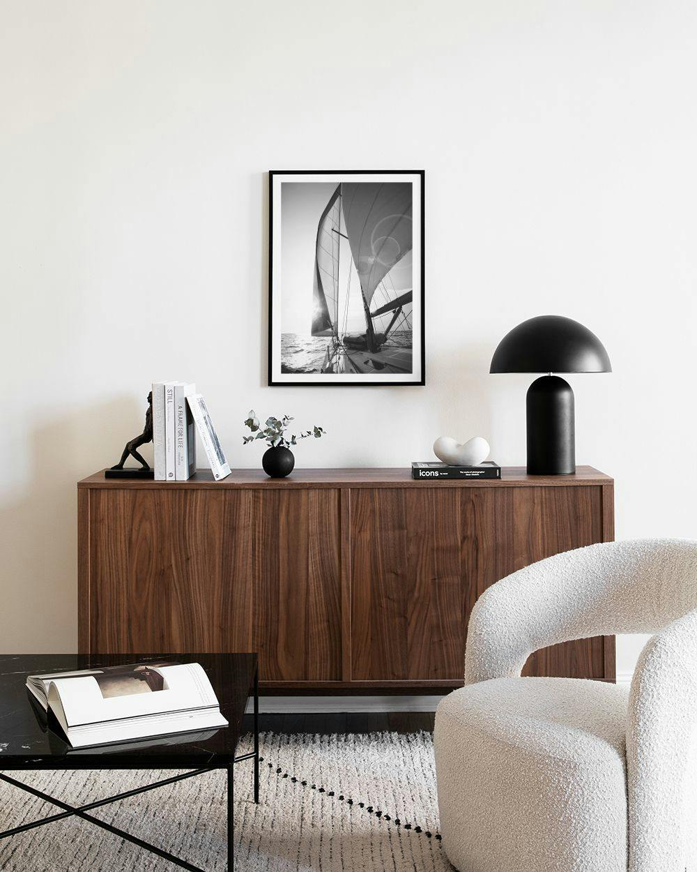 Affiche en noir et blanc dun voilier au coucher du soleil, affichée au-dessus dun buffet en bois.