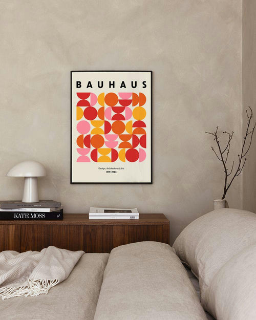 Affiche Bauhaus avec formes géométriques colorées, suspendue au-dessus dune table de chevet en bois dans une chambre.