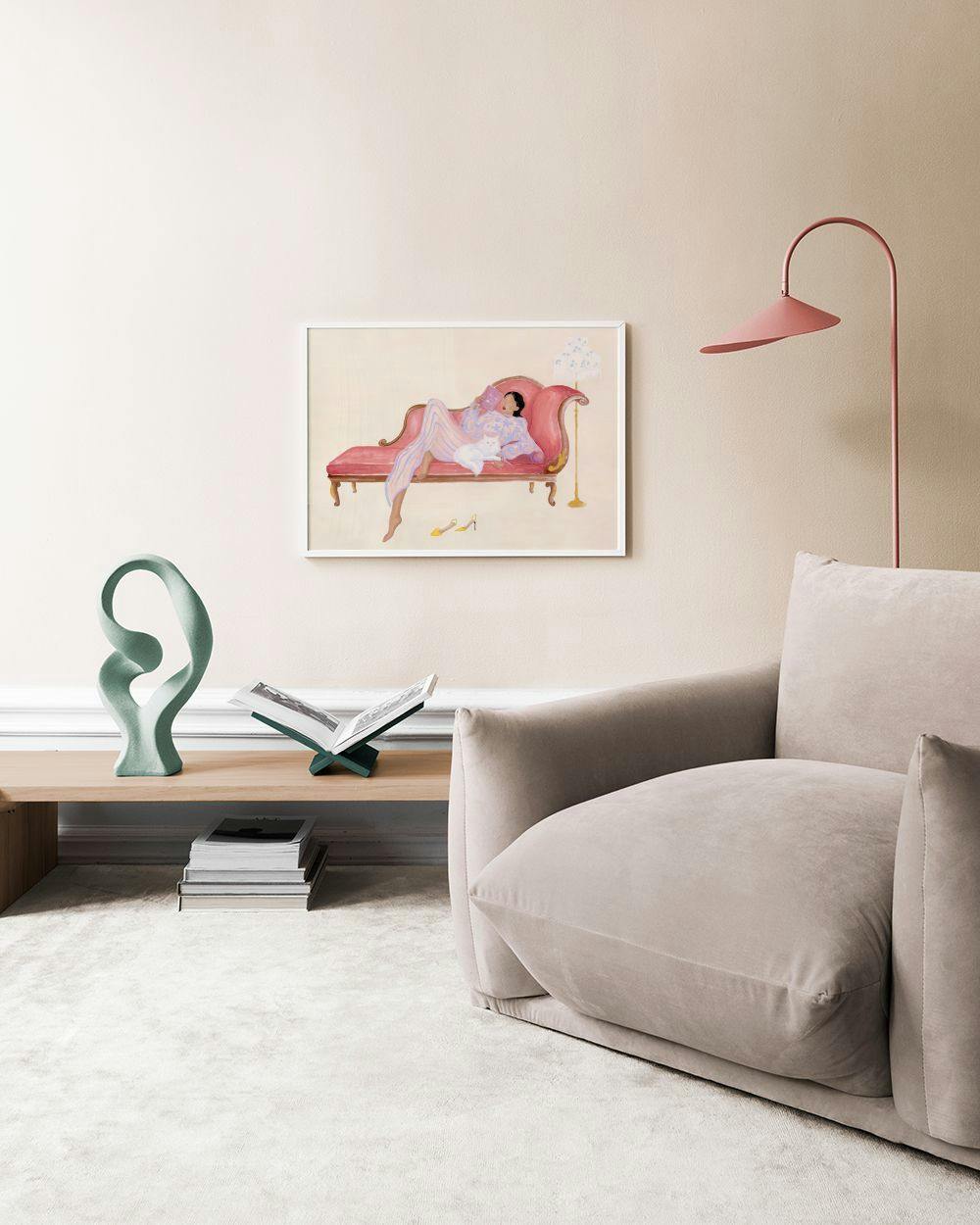 Affiche dune femme allongée sur une chaise longue rose avec un chat blanc, suspendue dans un salon moderne.