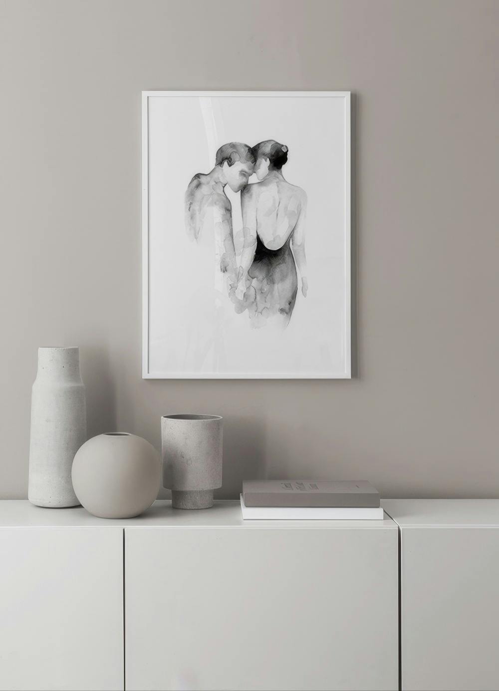 Affiche dun couple enlacé, en noir et blanc style aquarelle, suspendue au-dessus dun meuble blanc avec vases.