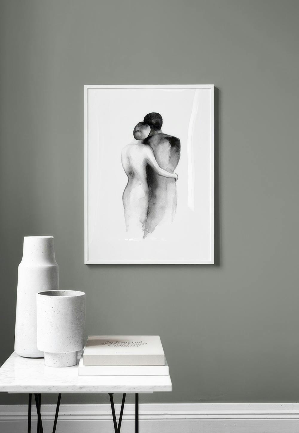 Affiche noire et blanche dun couple sembrassant, accrochée sur un mur gris au-dessus dune table avec des vases et des livres.