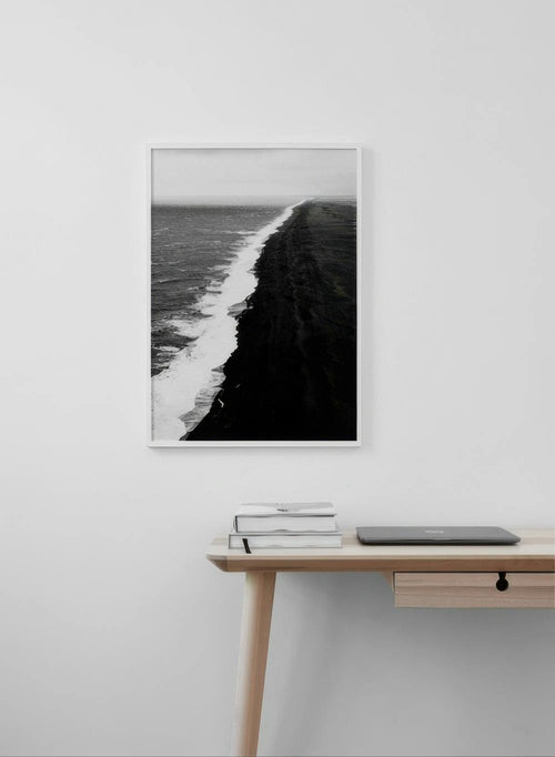 Affiche noir et blanc dune plage de sable noir et vagues déferlantes, suspendue au-dessus dun bureau en bois clair.