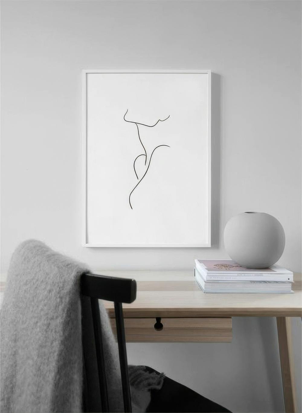 Affiche minimaliste de corps féminin en une seule ligne noire, accrochée au-dessus dun bureau en bois clair.