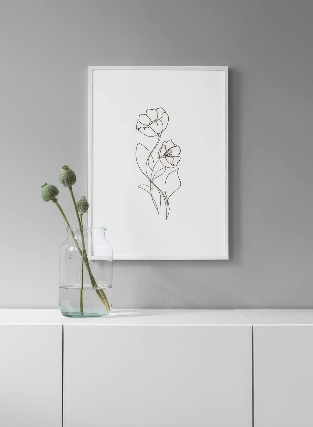 Affiche murale de dessin au trait noir de deux fleurs, suspendue au-dessus dun meuble blanc avec un vase.