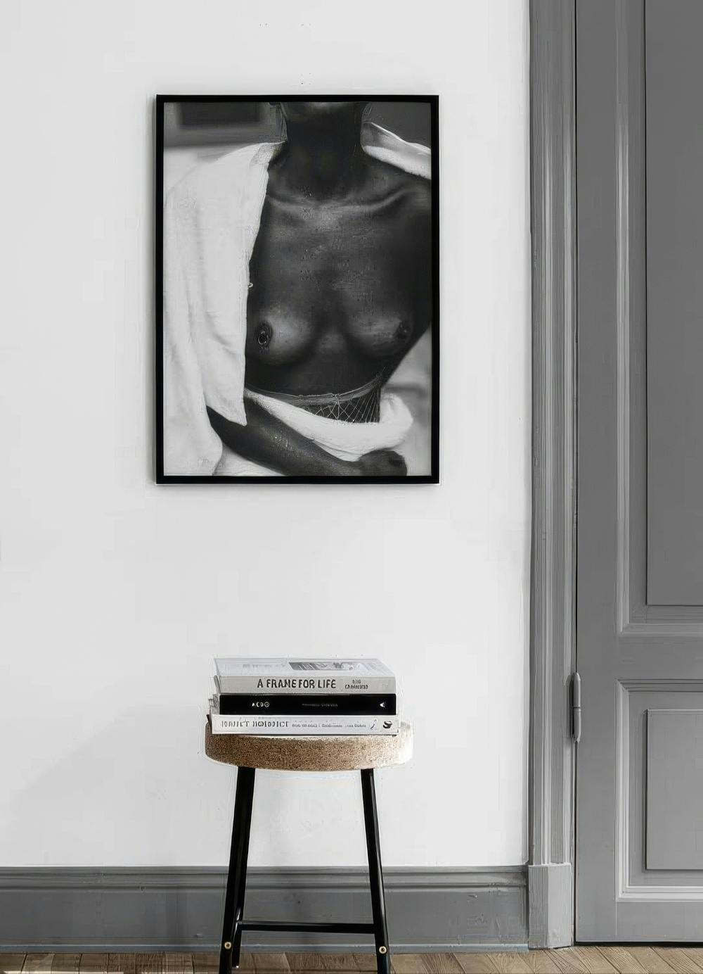 Affiche en noir et blanc dun buste féminin avec un tissu blanc, affichée au-dessus dun tabouret.