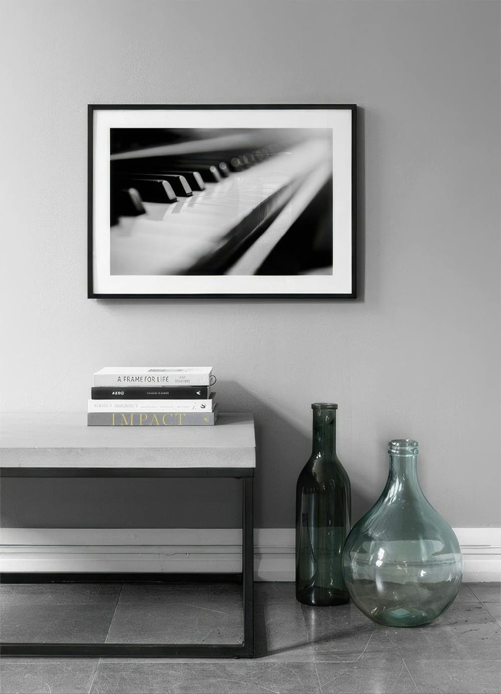 Affiche noire et blanche de touches de piano, suspendue au-dessus de livres et de vases dans un intérieur moderne.