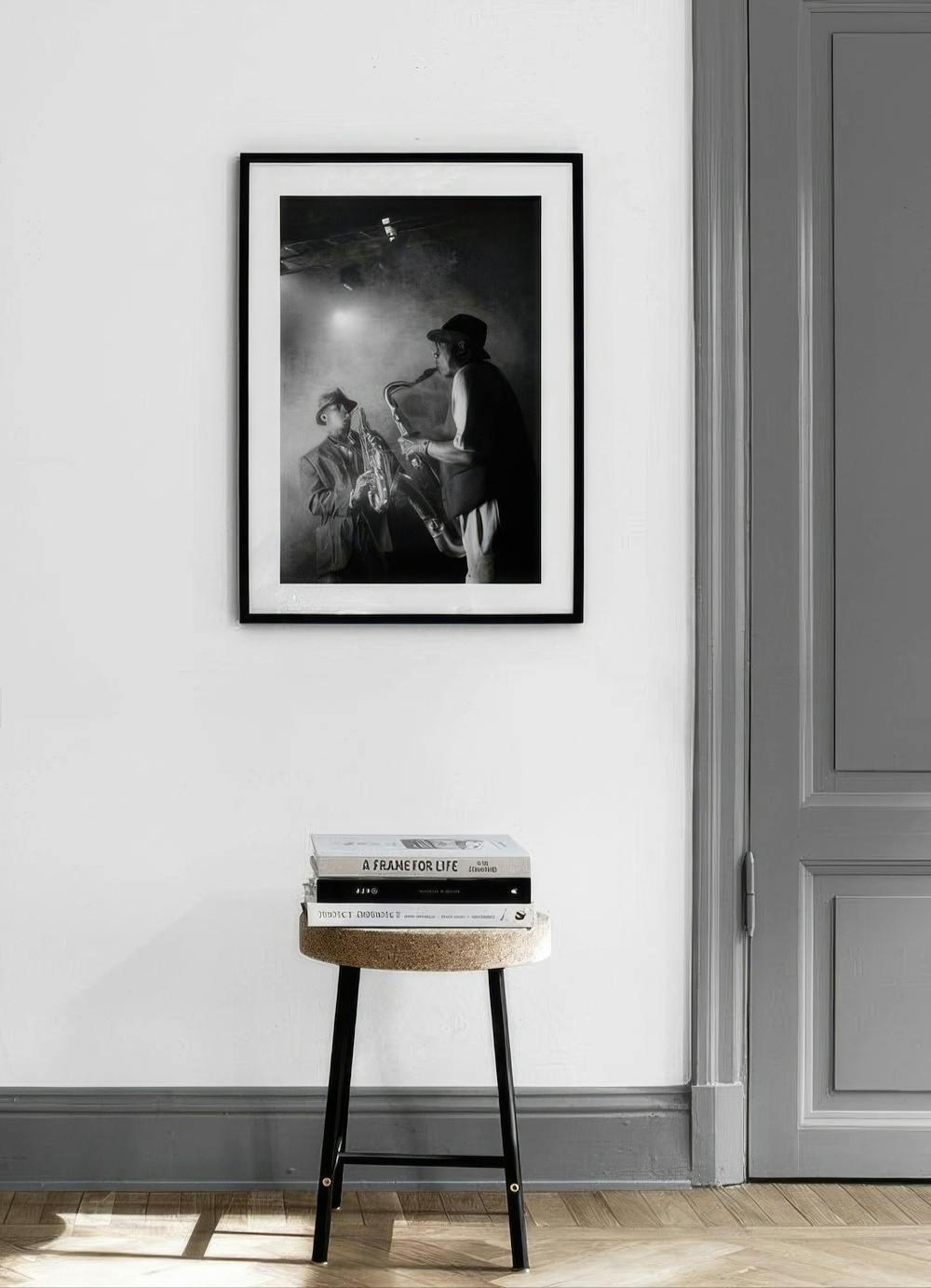 Affiche noir et blanc de deux saxophonistes de jazz, accrochée au mur blanc au-dessus dun tabouret avec des livres.