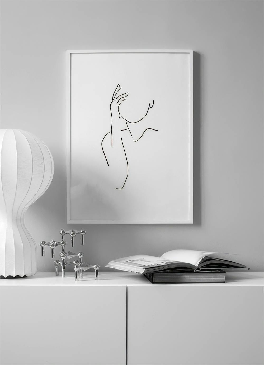 Affiche dun visage féminin abstrait en lignes noires au-dessus dun meuble blanc avec lampe et livres.