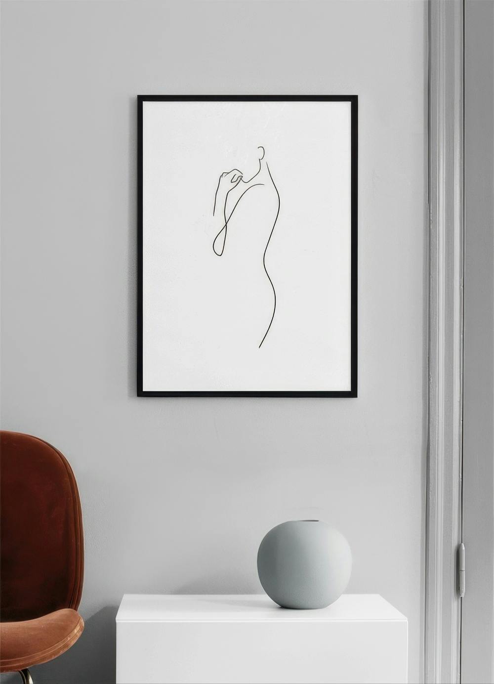 Affiche dune silhouette féminine en ligne continue, suspendue au-dessus dun meuble blanc avec un vase rond, et une chaise rouill