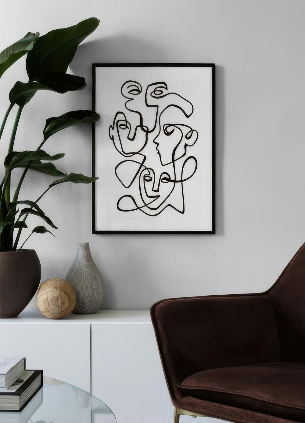 Affiche avec des visages abstraits en ligne noire, accrochée au mur au-dessus dun meuble blanc dans un salon moderne.