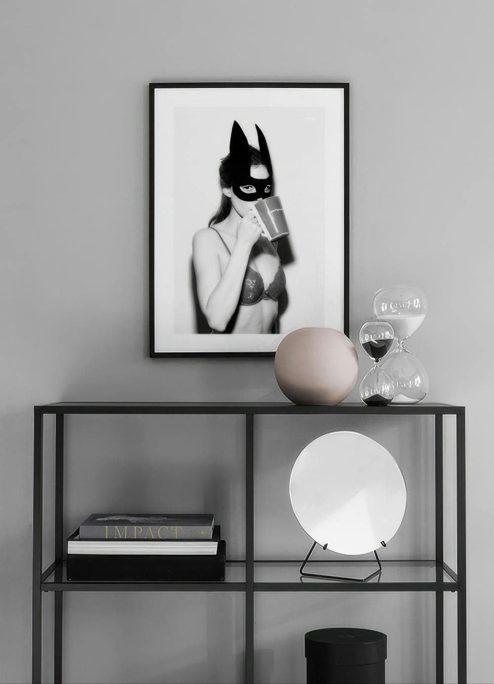 Affiche en noir et blanc dune femme en masque de chat et soutien-gorge buvant dans une tasse, accrochée au-dessus dune étagère n