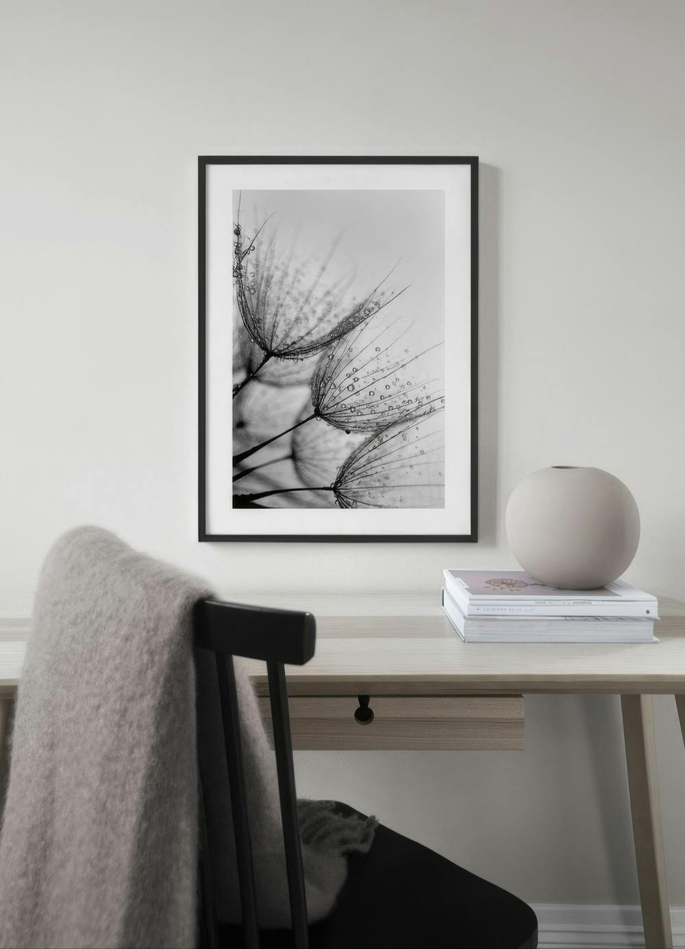 Affiche noir et blanc de pissenlits avec des gouttes deau, accrochée au-dessus dun bureau en bois avec une chaise.