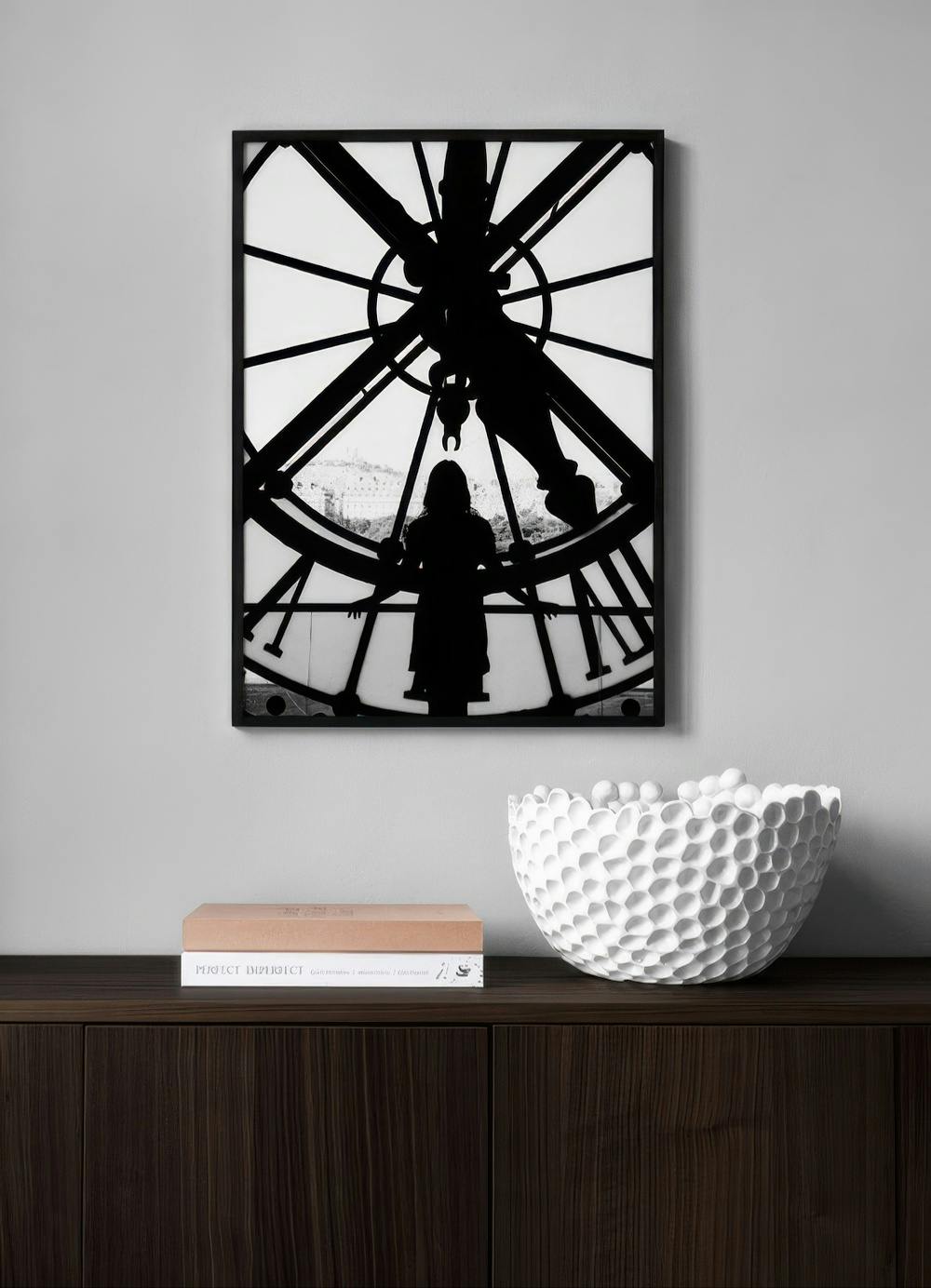 Affiche noir et blanc, silhouette dune personne devant une horloge géante, affichée au-dessus dun meuble en bois foncé.