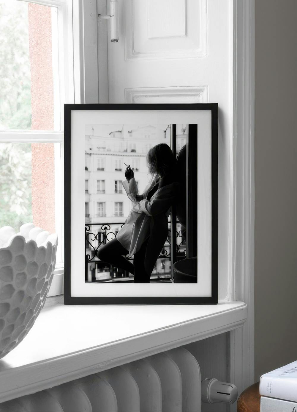 Affiche noir et blanc dune femme fumant sur un balcon parisien, posée sur un rebord de fenêtre blanc.