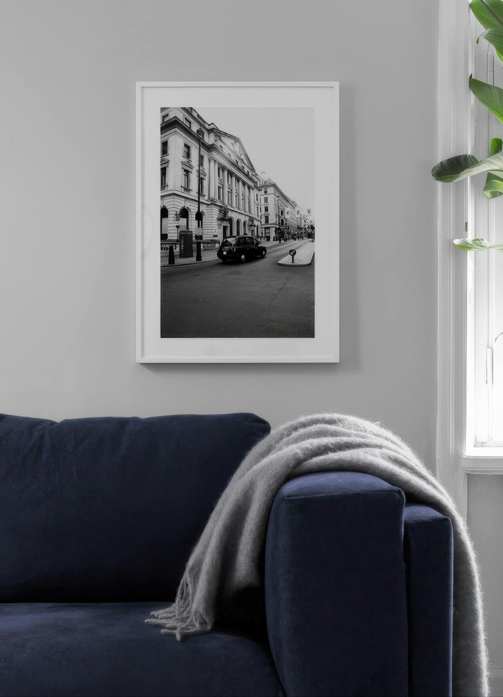 Affiche noir et blanc dune rue de Londres avec un taxi noir, accrochée au-dessus dun canapé bleu marine dans un salon moderne.