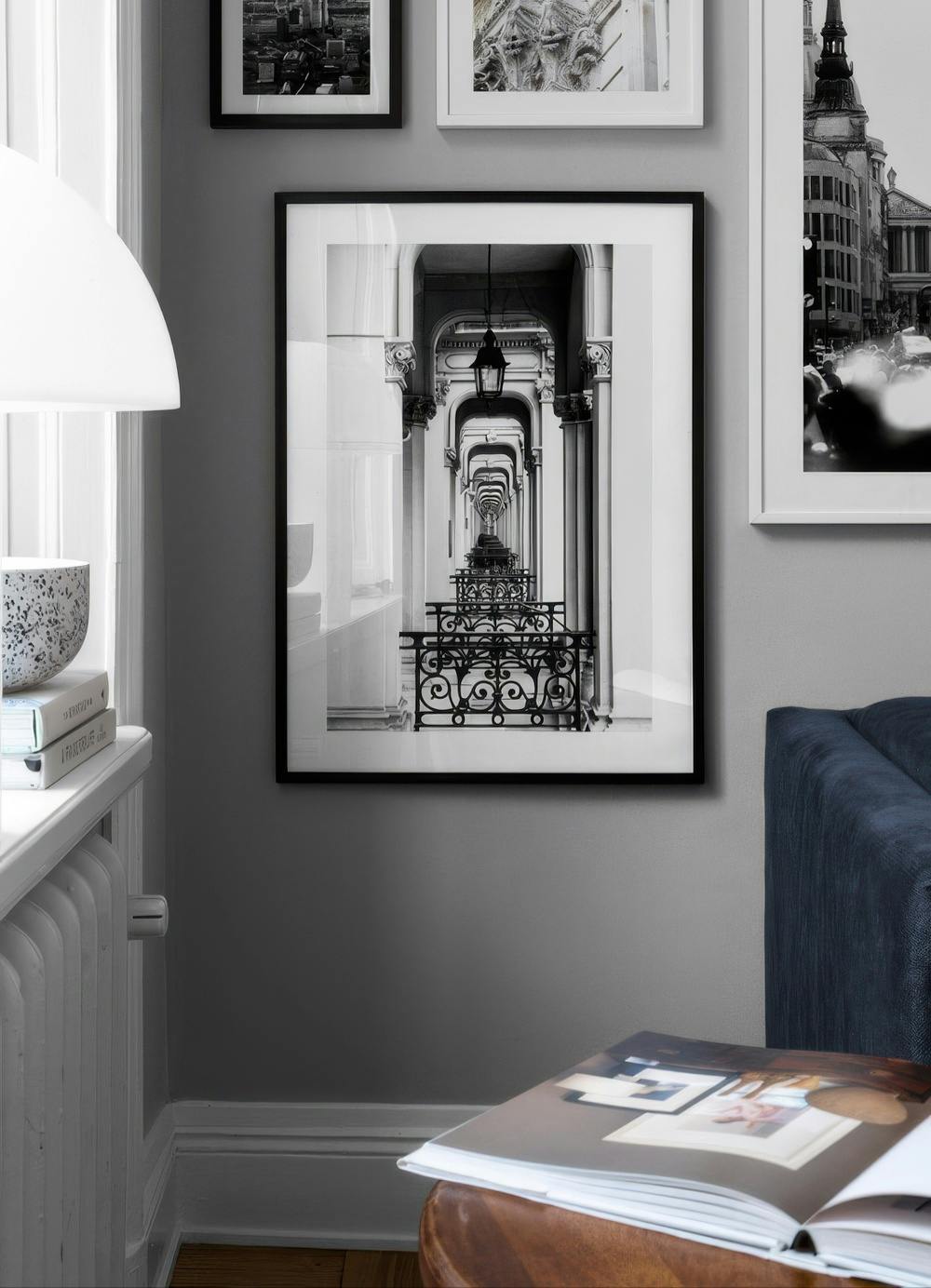 Affiche noir et blanc dune arcade avec balcons, accrochée dans un salon moderne au-dessus dun pouf en cuir.
