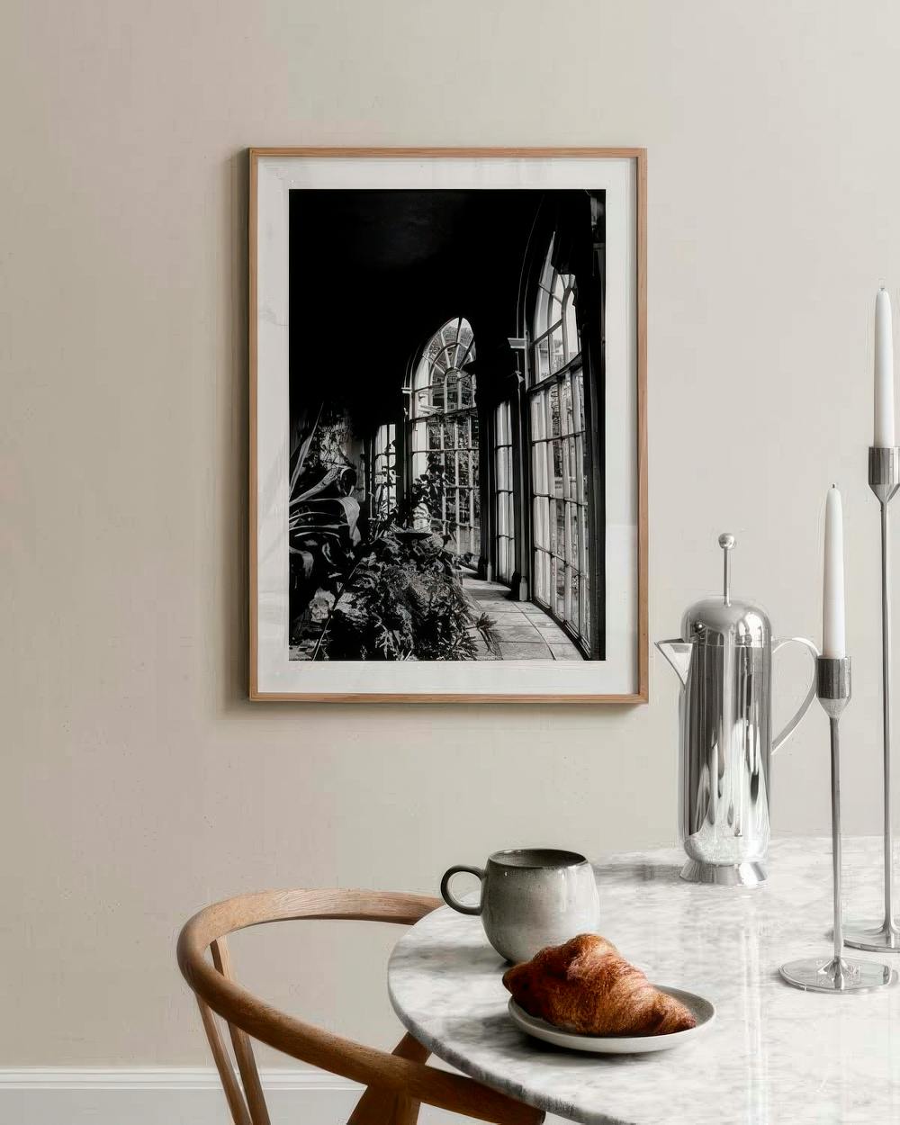 Affiche noir et blanc dun jardin dhiver avec grandes fenêtres, accrochée au mur près dune table en marbre.
