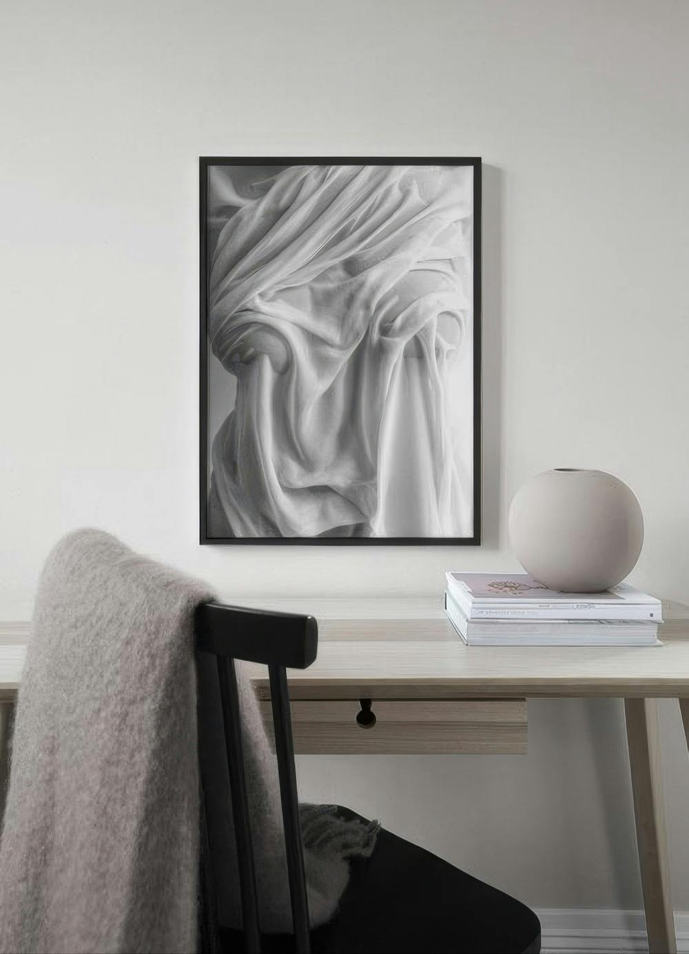 Affiche noir et blanc de drapés de tissu suspendue au-dessus dun bureau en bois clair avec une chaise.