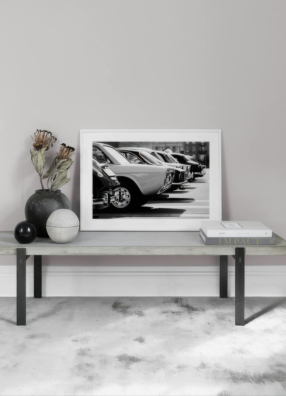 Affiche en noir et blanc de voitures de collection alignées, posée sur un banc gris dans un salon minimaliste.