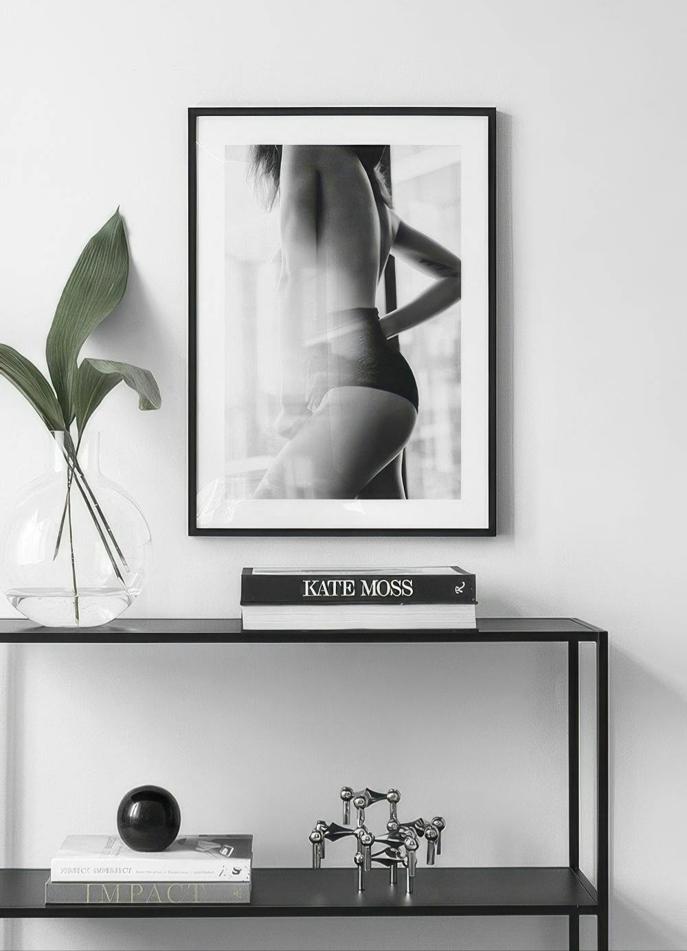Affiche en noir et blanc dune femme en lingerie, accrochée au-dessus dune console noire avec des livres et des objets.