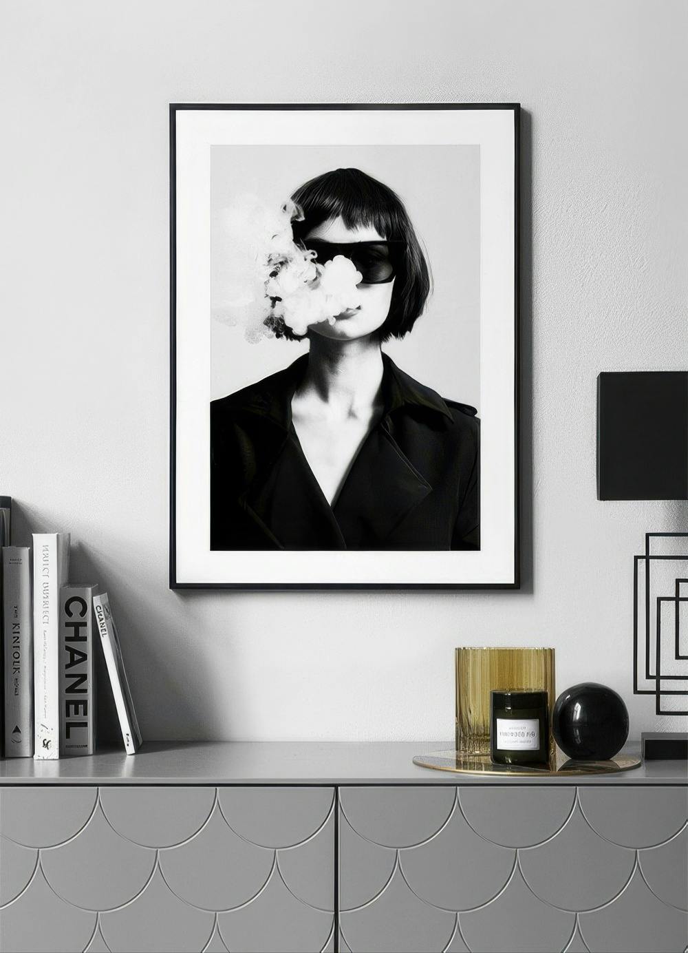 Affiche en noir et blanc d’une femme aux lunettes de soleil, de la fumée sortant de sa bouche, suspendue au-dessus dun buffet.