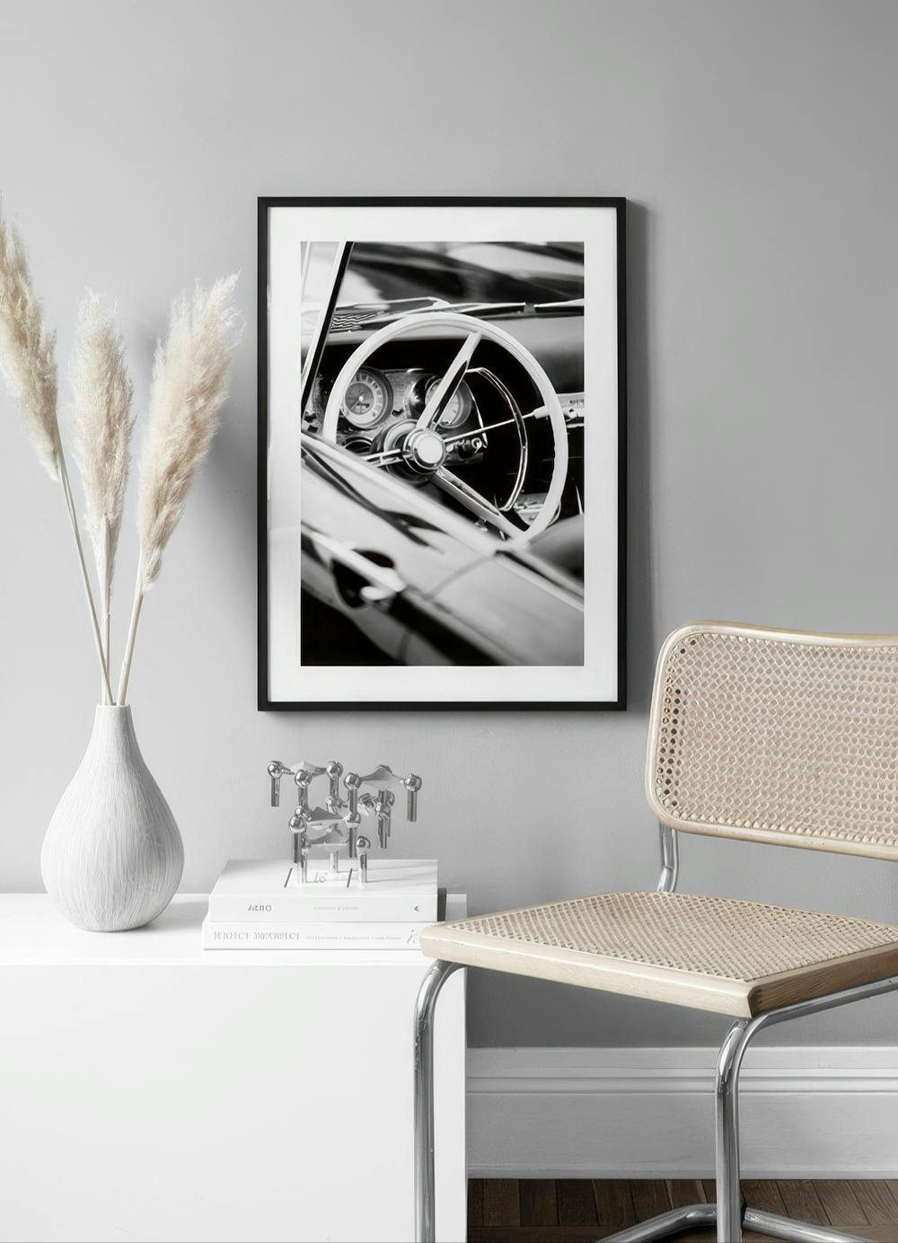 Affiche en noir et blanc dun intérieur de voiture vintage, exposée sur un mur gris clair avec un fauteuil en bois.