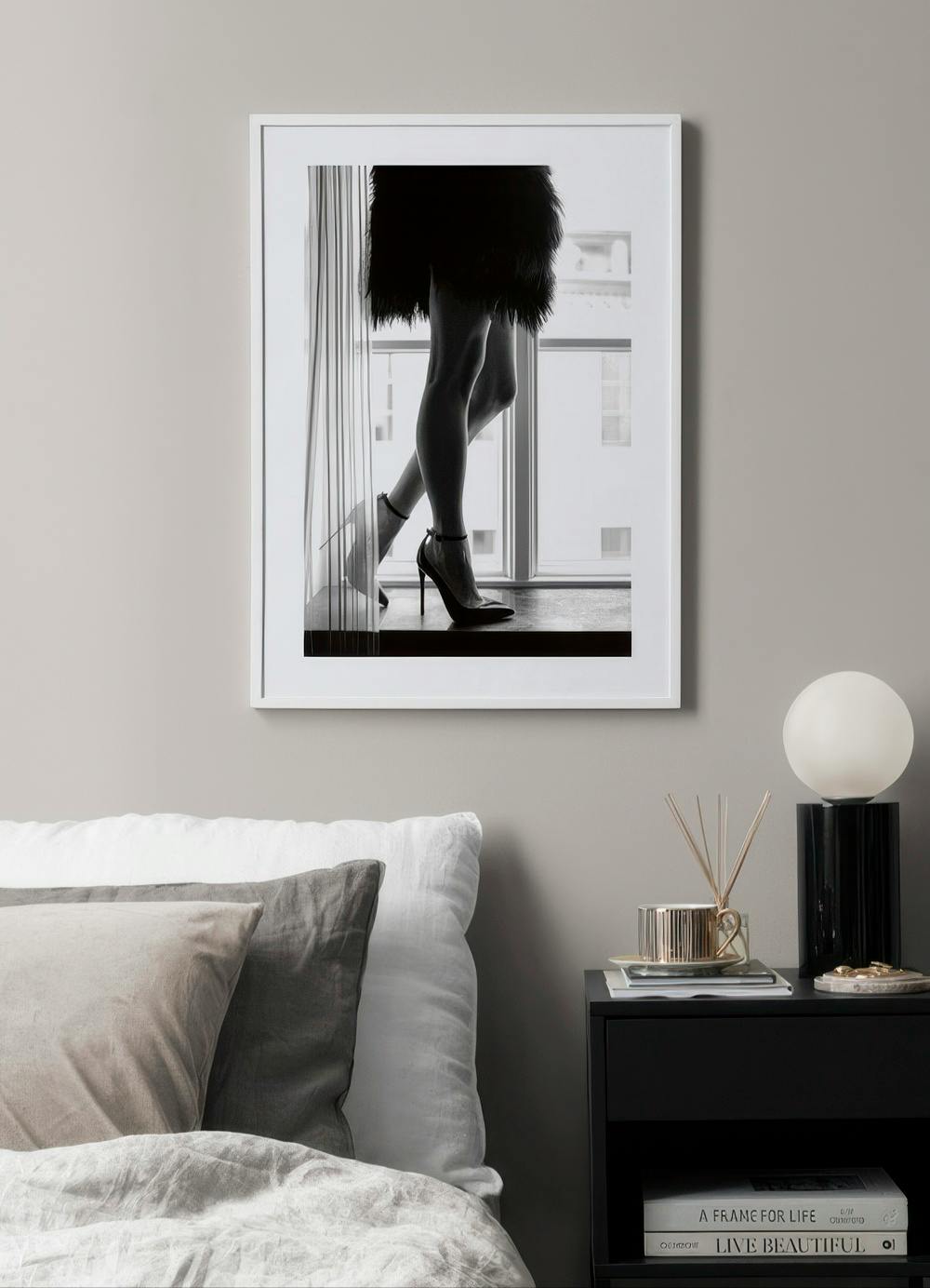 Affiche noir et blanc de jambes féminines en talons hauts, posée sur une table de chevet dans une chambre.