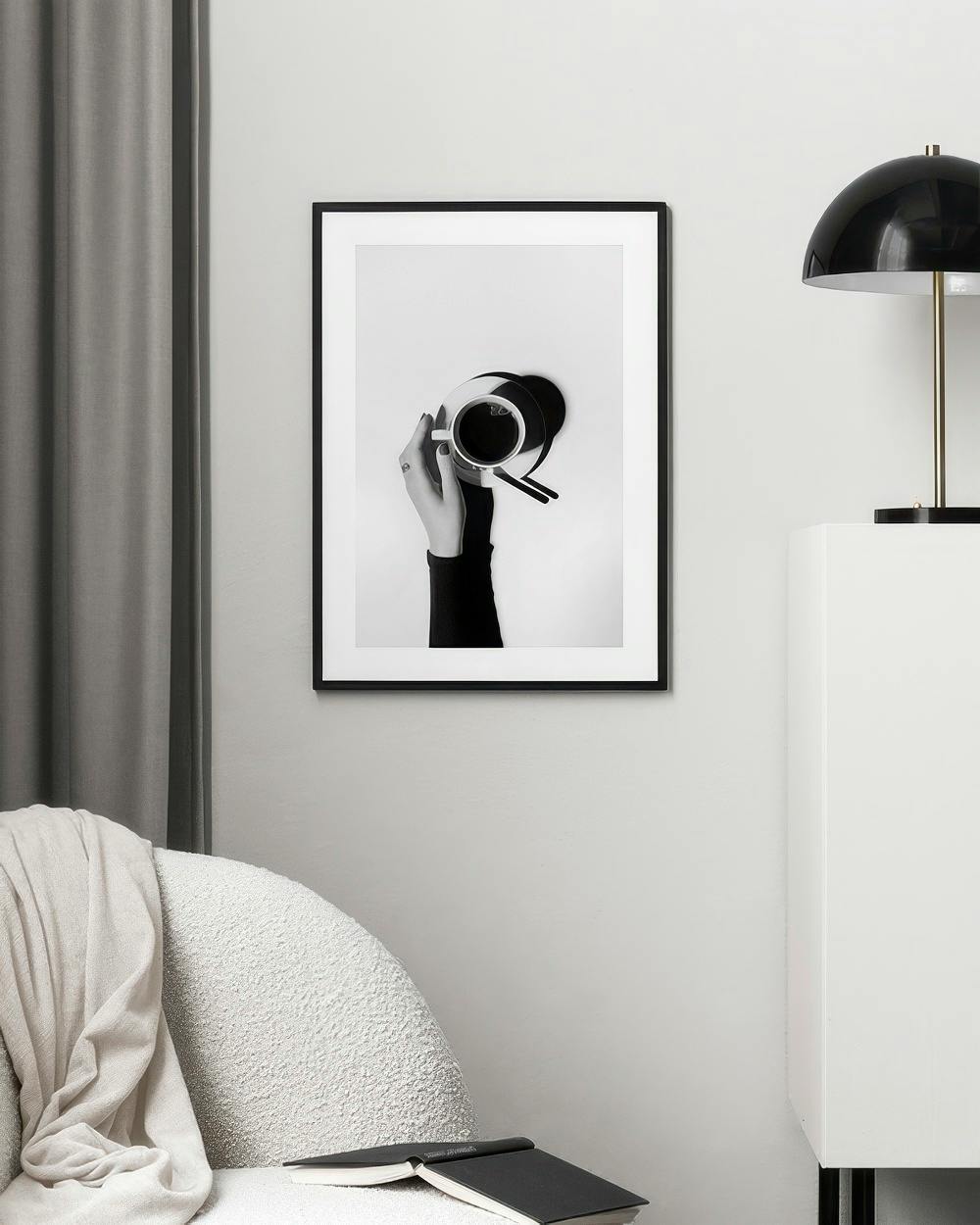 Affiche photo en noir et blanc dune main tenant une tasse de café, accrochée dans un salon moderne.