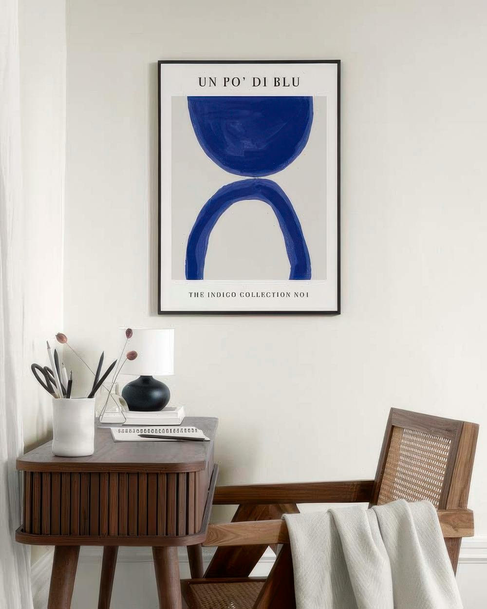 Affiche Un Po Di Blu avec formes abstraites indigo, suspendue au-dessus dune commode et dun fauteuil en bois.
