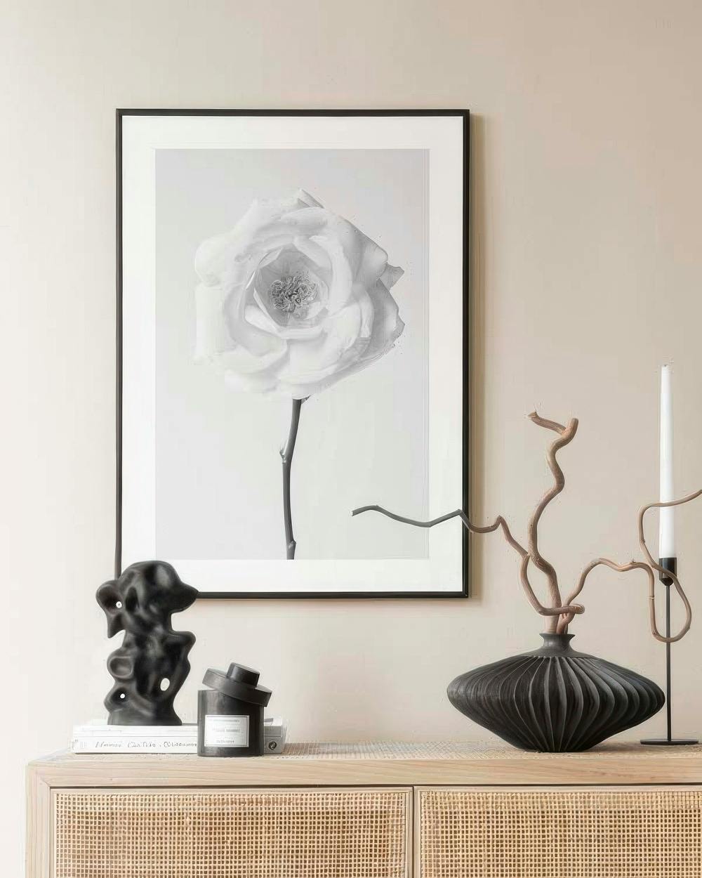 Affiche murale en noir et blanc dune rose sur un buffet en rotin, dans un intérieur moderne.