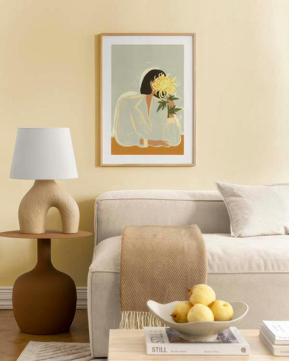 Affiche dune femme tenant une fleur jaune, accrochée au-dessus dun canapé dans un salon lumineux.