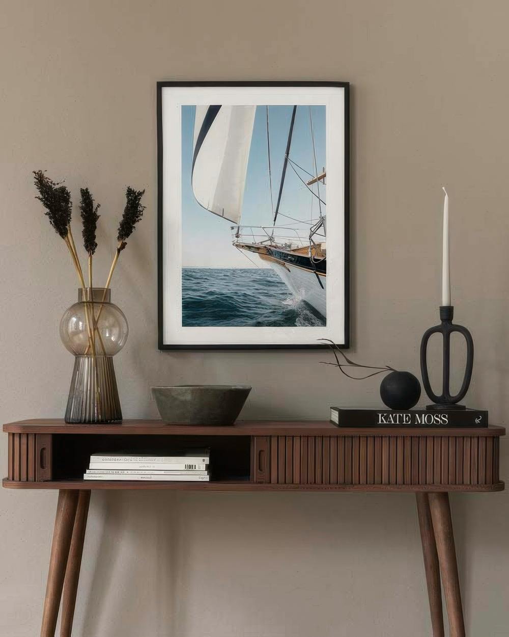 Affiche dun voilier sur leau, exposée au-dessus dune console en bois avec vase et bougeoir.