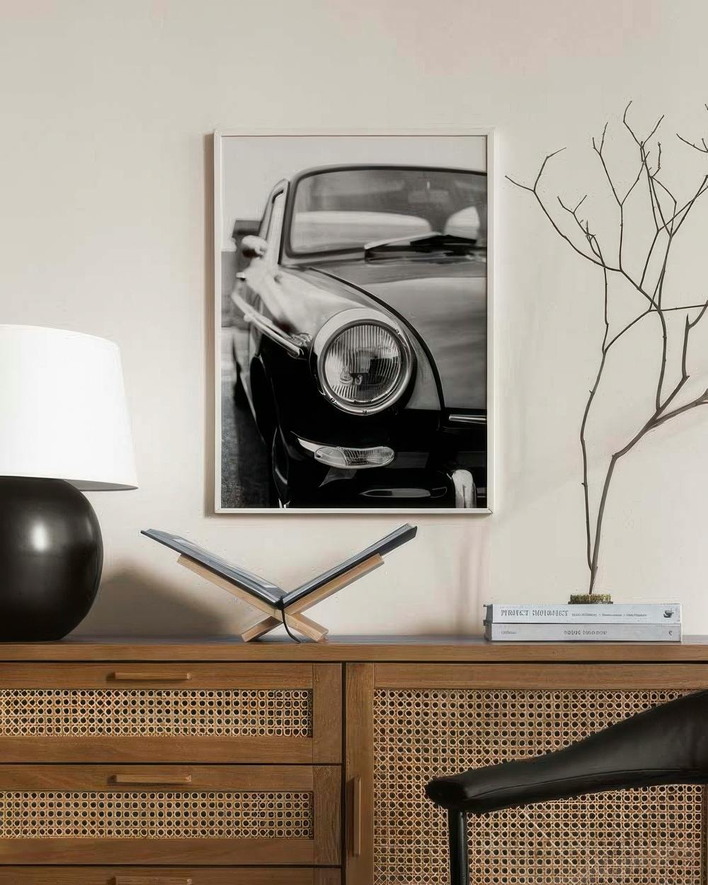 Affiche noir et blanc dune voiture vintage, accrochée au-dessus dun buffet en bois clair avec une lampe et des objets décoratifs