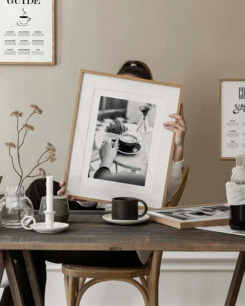 Affiche noir et blanc dune main tenant une tasse de café, avec un croissant, sur une table en bois rustique.