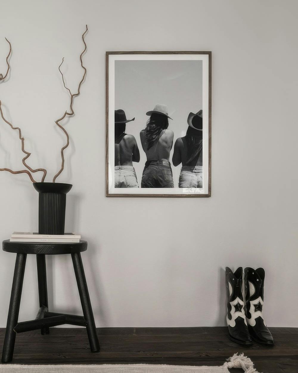 Affiche en noir et blanc de trois femmes en chapeaux de cowboy et shorts, suspendue dans un intérieur contemporain.