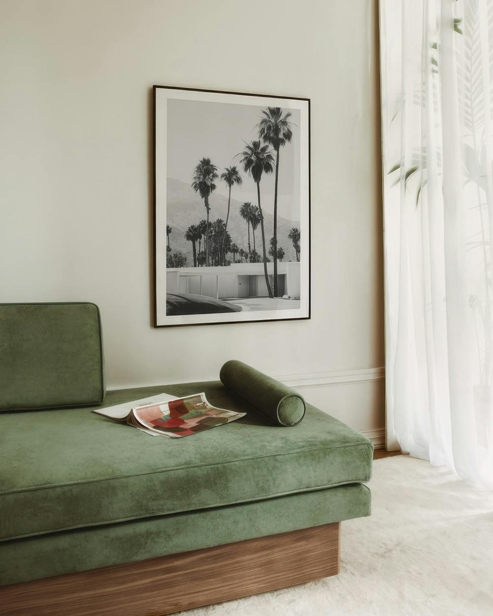 Affiche noir et blanc de palmiers et dune maison moderne, accrochée au-dessus dun canapé vert.