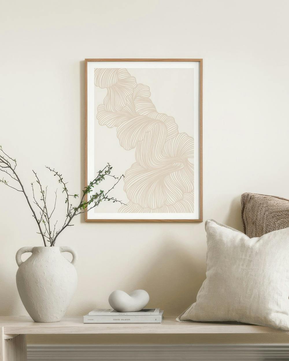 Affiche de formes organiques beiges et ondulées, accrochée au-dessus dun banc avec un vase et des coussins.