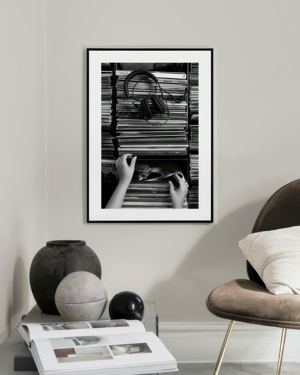 Affiche noir et blanc de mains cherchant un vinyle dans une collection, avec des écouteurs, affichée dans un salon moderne.