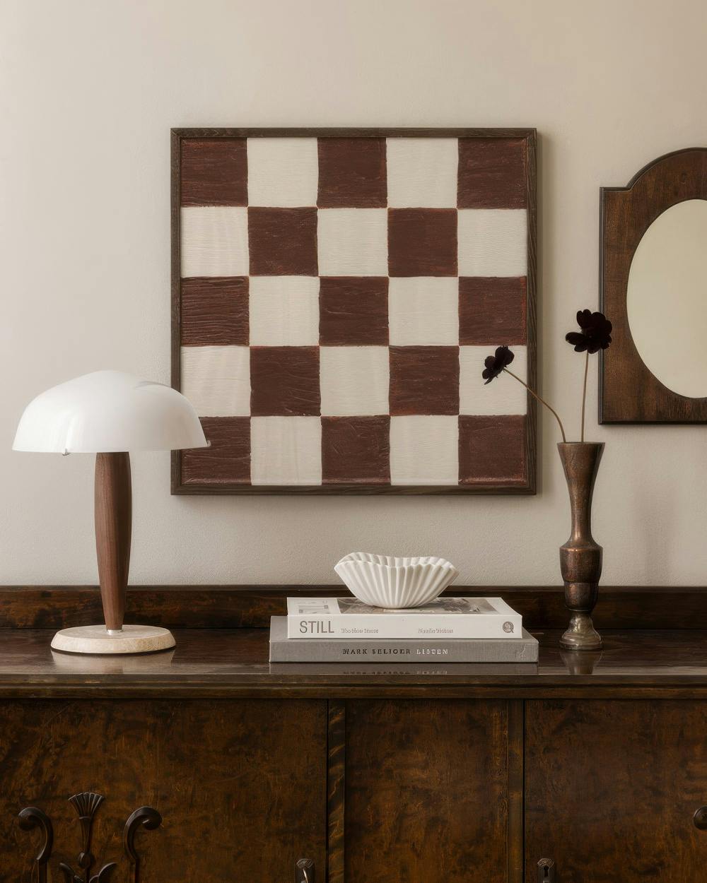 Affiche échiquier marron et blanc sur un mur clair, au-dessus dun buffet en bois, à côté dune lampe et dun vase.