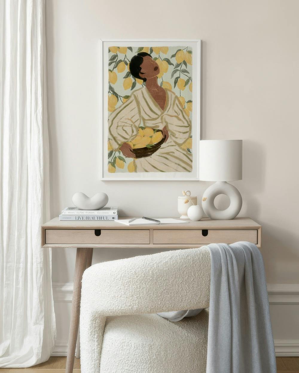 Affiche dune femme tenant un panier de citrons, suspendue au-dessus dun bureau en bois clair dans un salon moderne.
