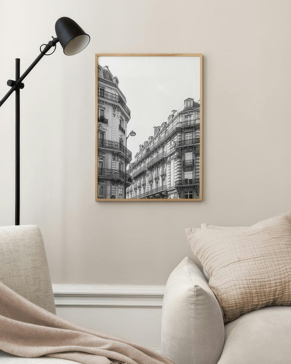 Affiche noir et blanc de bâtiments haussmanniens de Paris, accrochée au-dessus dun canapé beige avec coussin.
