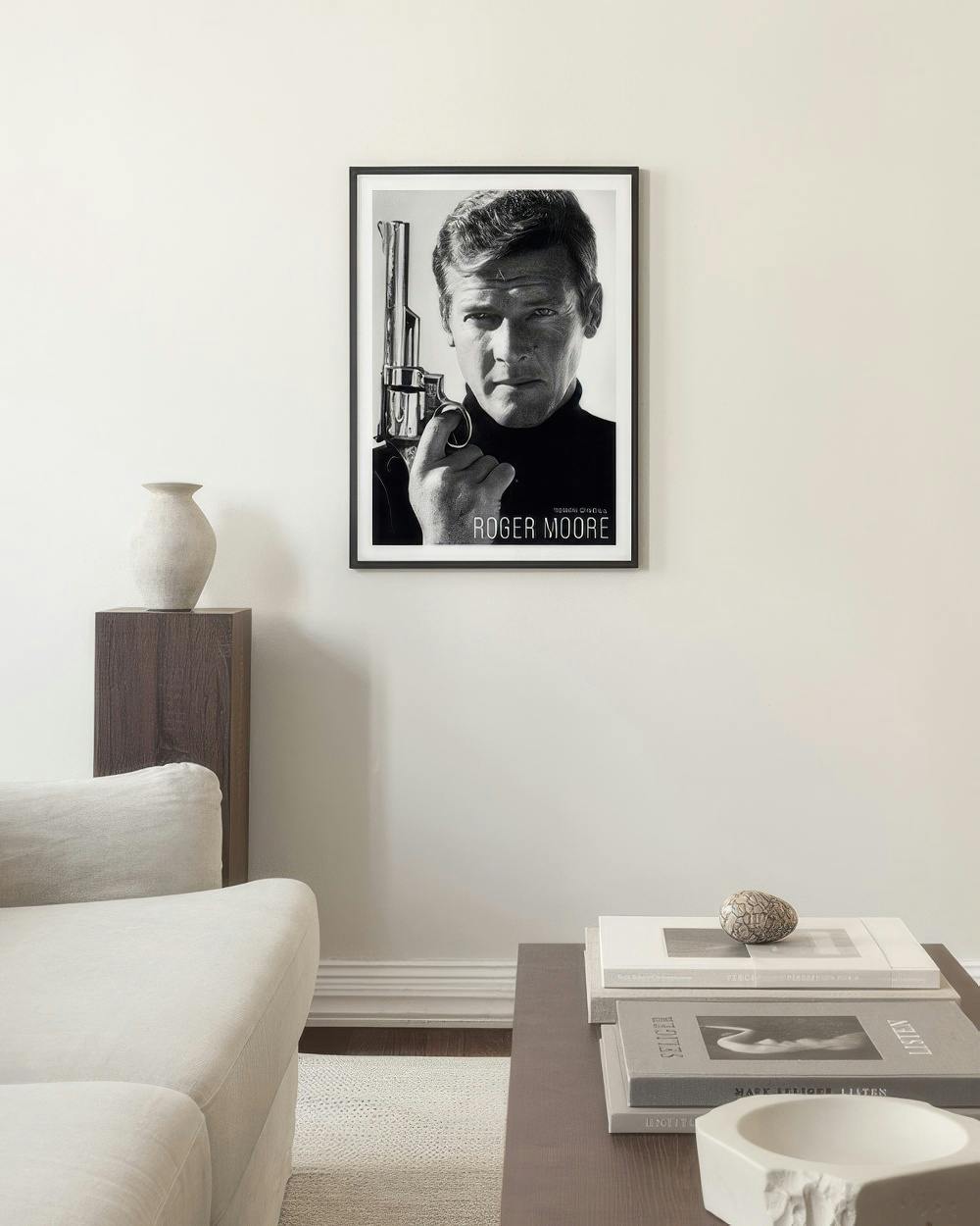 Affiche de Roger Moore en noir et blanc avec un pistolet, affichée dans un salon moderne au-dessus dune table basse.