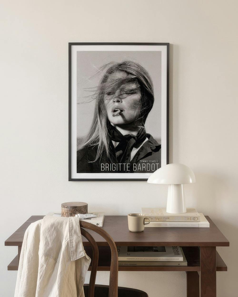 Affiche noir et blanc de Brigitte Bardot, cheveux au vent, fumant, affichée au-dessus dun bureau en bois.