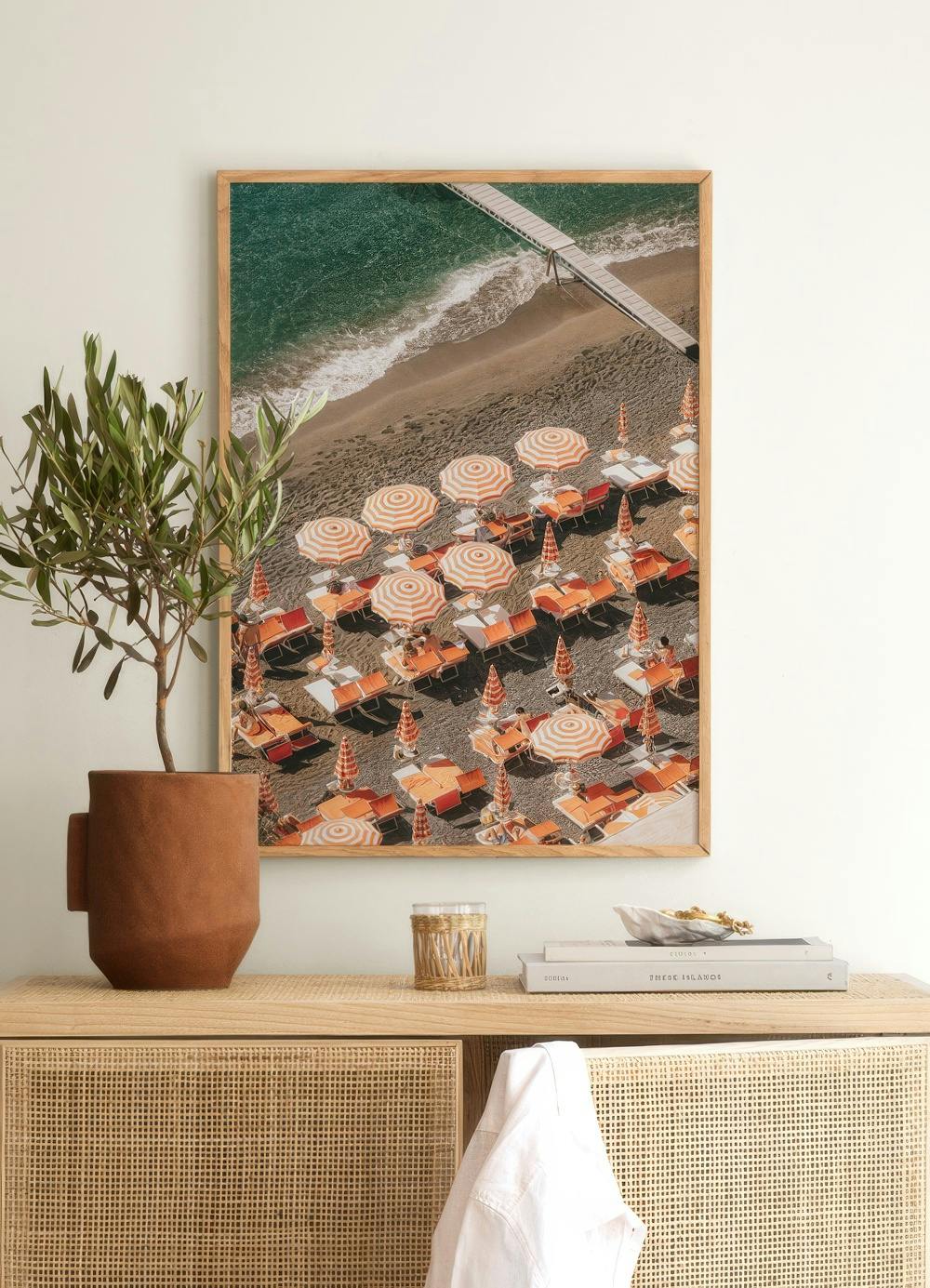 Affiche vue aérienne dune plage avec parasols rayés orange et blancs, suspendue au-dessus dun meuble en rotin.