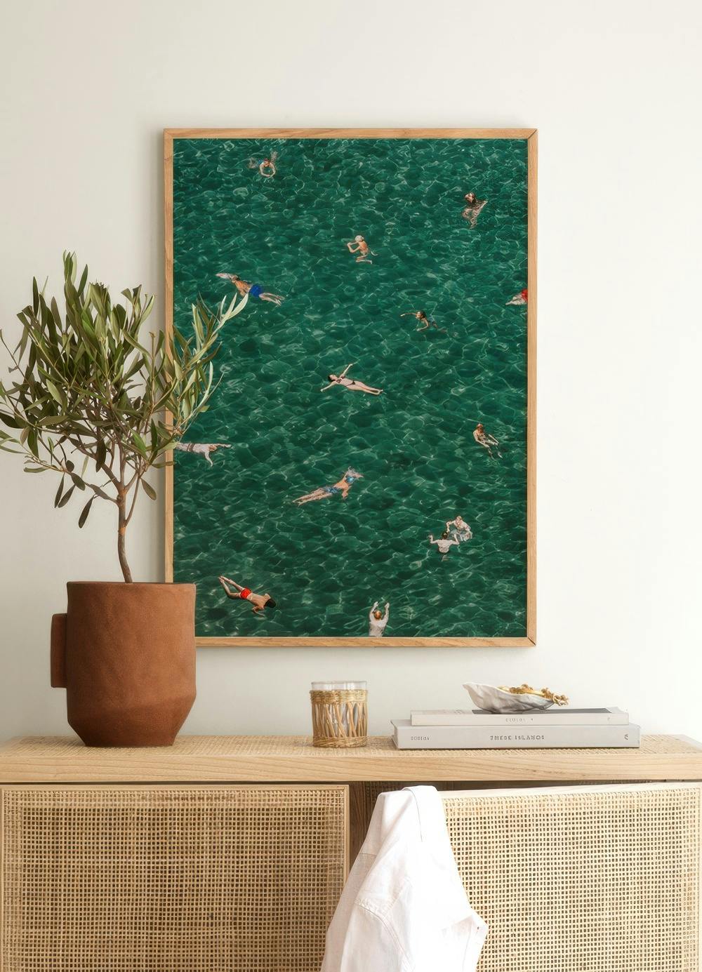 Affiche avec vue aérienne de personnes nageant dans une eau turquoise, suspendue au-dessus dun meuble en rotin clair.