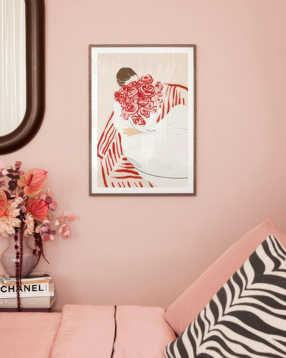 Affiche dune femme tenant un bouquet de roses rouges, suspendue sur un mur rose au-dessus dun canapé.