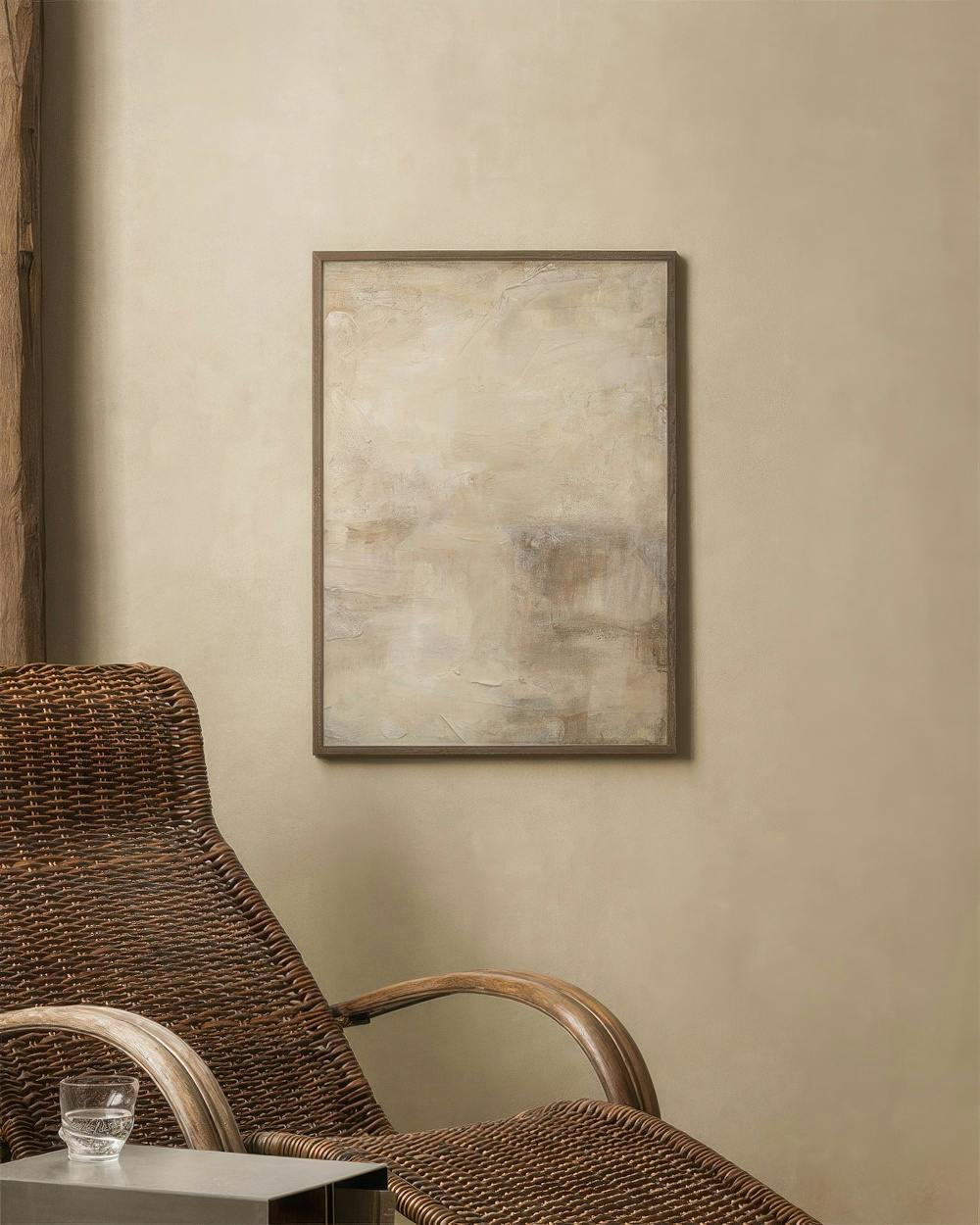 Affiche aux tons neutres, beige et marron, avec des coups de pinceau texturés, affichée au-dessus dun fauteuil en rotin.