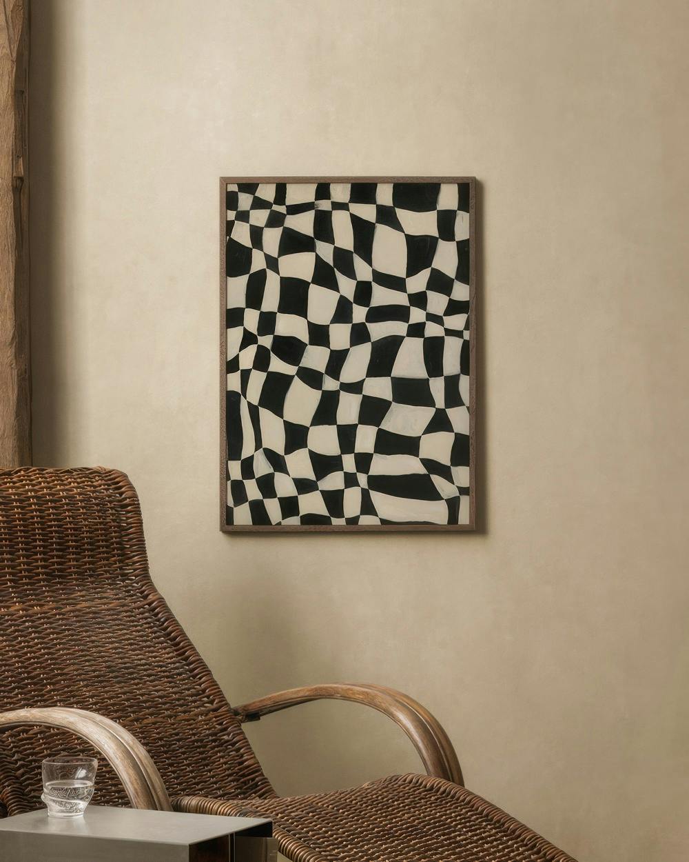 Affiche au motif damier déformé noir et blanc, accrochée au mur au-dessus dun fauteuil en rotin.