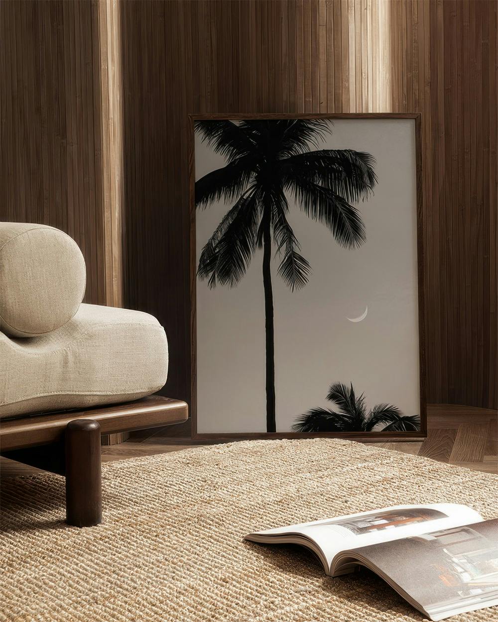 Affiche avec un palmier noir et une lune sur fond clair, posée sur un parquet près dun canapé beige.