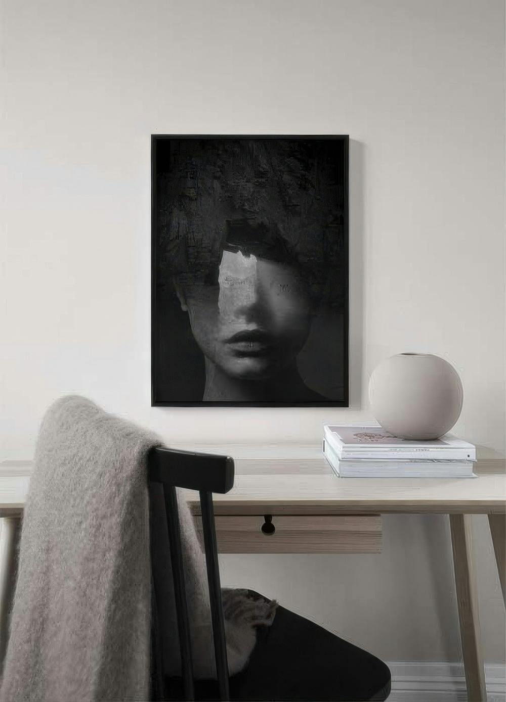 Affiche dun visage féminin sombre, la partie supérieure texturée, suspendue au-dessus dun bureau en bois clair.